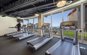 A gym with treadmills and exercise equipment, large windows with a view of the ocean and buildings. - The Gulf Perch - 3BR - Beach Views & Resort Pools (Panama City Beach)