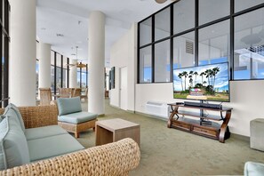 A spacious lobby with a large window, wicker furniture, and a flat-screen TV. - Sunchase IV #312 - Beachfront Resort, Pools & Balcony (South Padre Island)