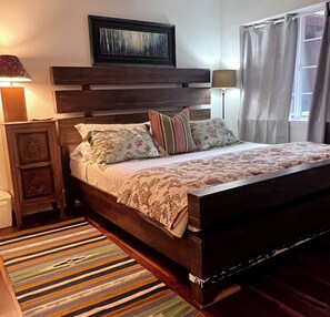 A bed with a wooden headboard, a patterned bedspread, and multiple pillows. There is a nightstand with a lamp, a window with curtains, and a wall-mounted artwork above the bed. - Live Like a Local in this Spacious Ground Level Condo -close to Dining & Skiing❄️ (Edwards)