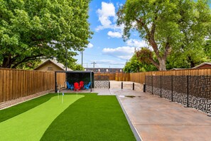 A backyard with artificial grass, a covered seating area with chairs, and a wooden fence. - Stylish Japandi 1BR-Bishop Arts-Nr Downtown Dallas (Dallas)