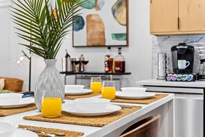 A breakfast setting with a white table, plates, glasses, and a clear glass vase with green leaves. - Stylish Japandi 1BR-Bishop Arts-Nr Downtown Dallas (Dallas)