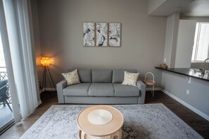 A living room with a grey sofa, a coffee table, a floor lamp, and a kitchen area with a sink and countertop. - Cozy 1-bedroom apartment in Marina del Rey (Marina del Rey)