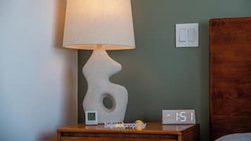 A nightstand with a lamp, a digital clock, and a wall switch.