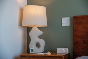 A nightstand with a lamp, a digital clock, and a wall switch. - Amazing 2BR Condo with Rooftop Pool, Gym and Views (Cabo San Lucas)