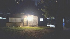 A small, single-story building with a lit window and a door, surrounded by trees. - Modern Tulsa Retreat  Stylish 3BR Home Near Downtown & Local Attractions (Tulsa)