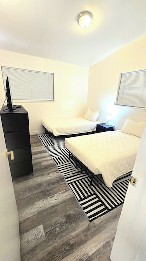 Een hotelkamer met twee bedden, een dressoir, een televisie en een raam met jaloezieën.
