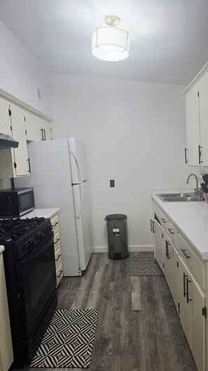 A compact kitchen with white cabinets, a black stove, a white refrigerator, and a trash bin. - Modern Tulsa Retreat  Stylish 3BR Home Near Downtown & Local Attractions (Tulsa)