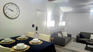 A room with a dining table set for four, a sofa, a chair, and a clock on the wall. - Modern Tulsa Retreat  Stylish 3BR Home Near Downtown & Local Attractions (Tulsa)