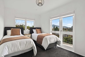 A bedroom with two beds, a large window, and a view of the outdoors. - The White Terraces - Spa Pool, Sleeps 10 (Rotorua)