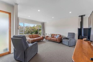 A spacious living area with a sofa set, a chair, a coffee table, and a fireplace. - Huia Nest - Walk to Golf & Stadium, Sleeps 8 (Rotorua)