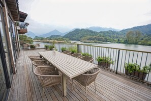 A wooden deck with a table and chairs overlooking a river and mountains. - ZHU85 (Lishui)