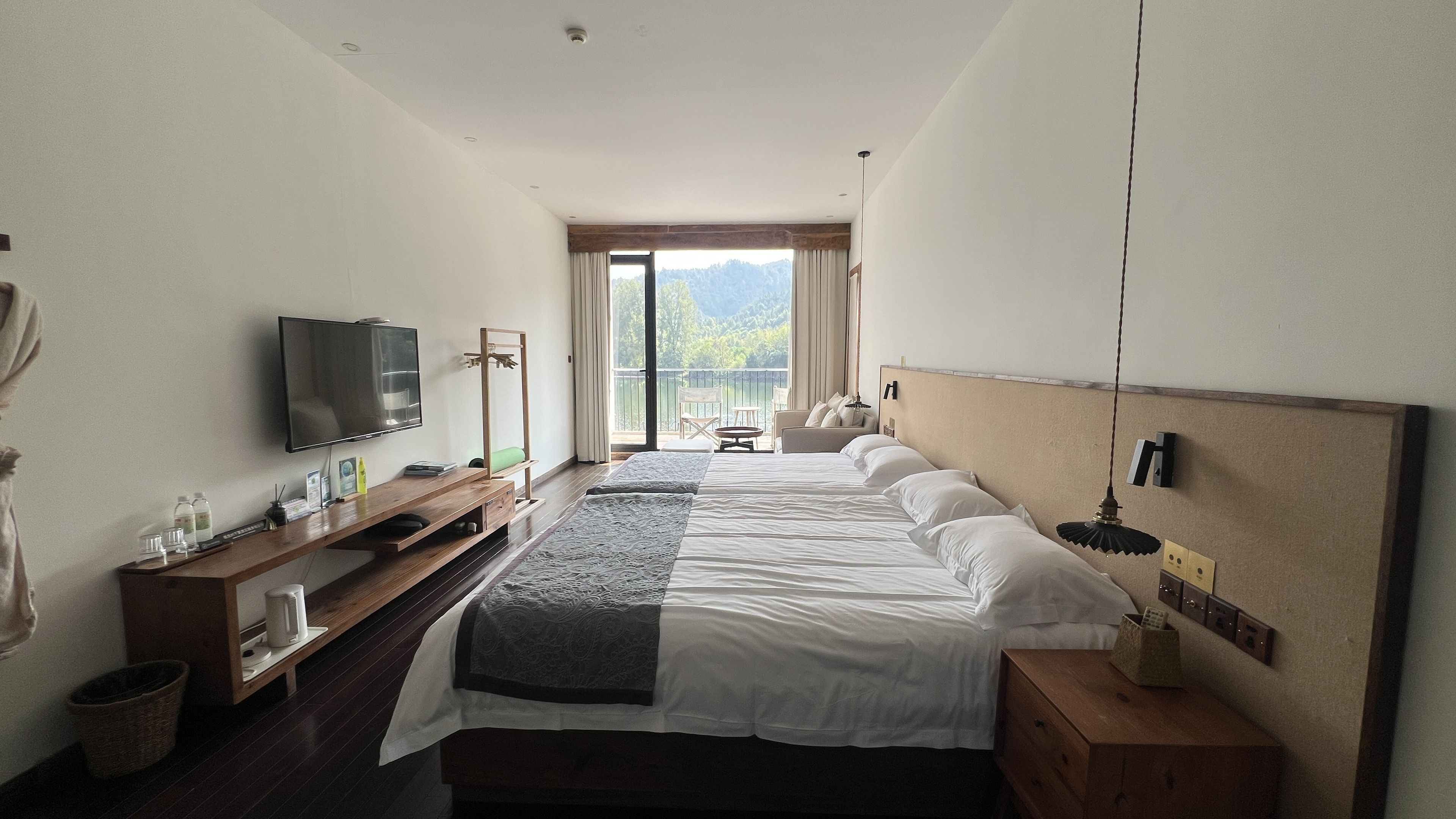 Ein Hotelzimmer mit einem Bett, einem Fernseher, einem Schreibtisch mit Computer und einem Balkon mit Bergblick.