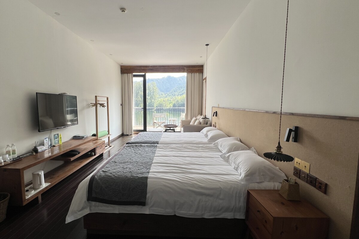 A hotel room with a bed, a TV, a desk with a computer, and a balcony with a view of the mountains.