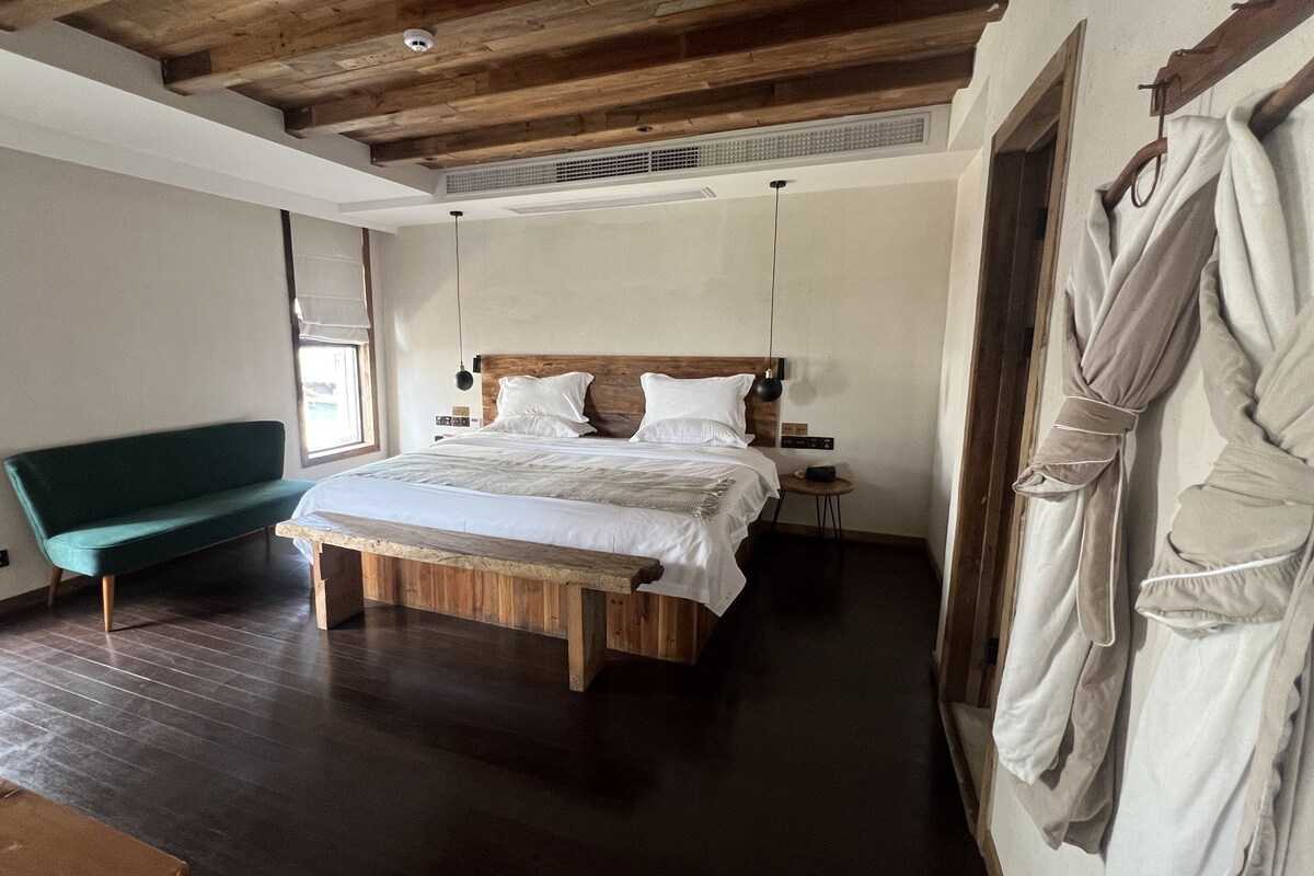 A room with a bed, a bench, a robe rack, and a window.