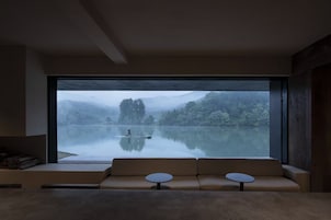 Interior moderno com uma janela ampla que dá para um lago calmo e uma floresta.
