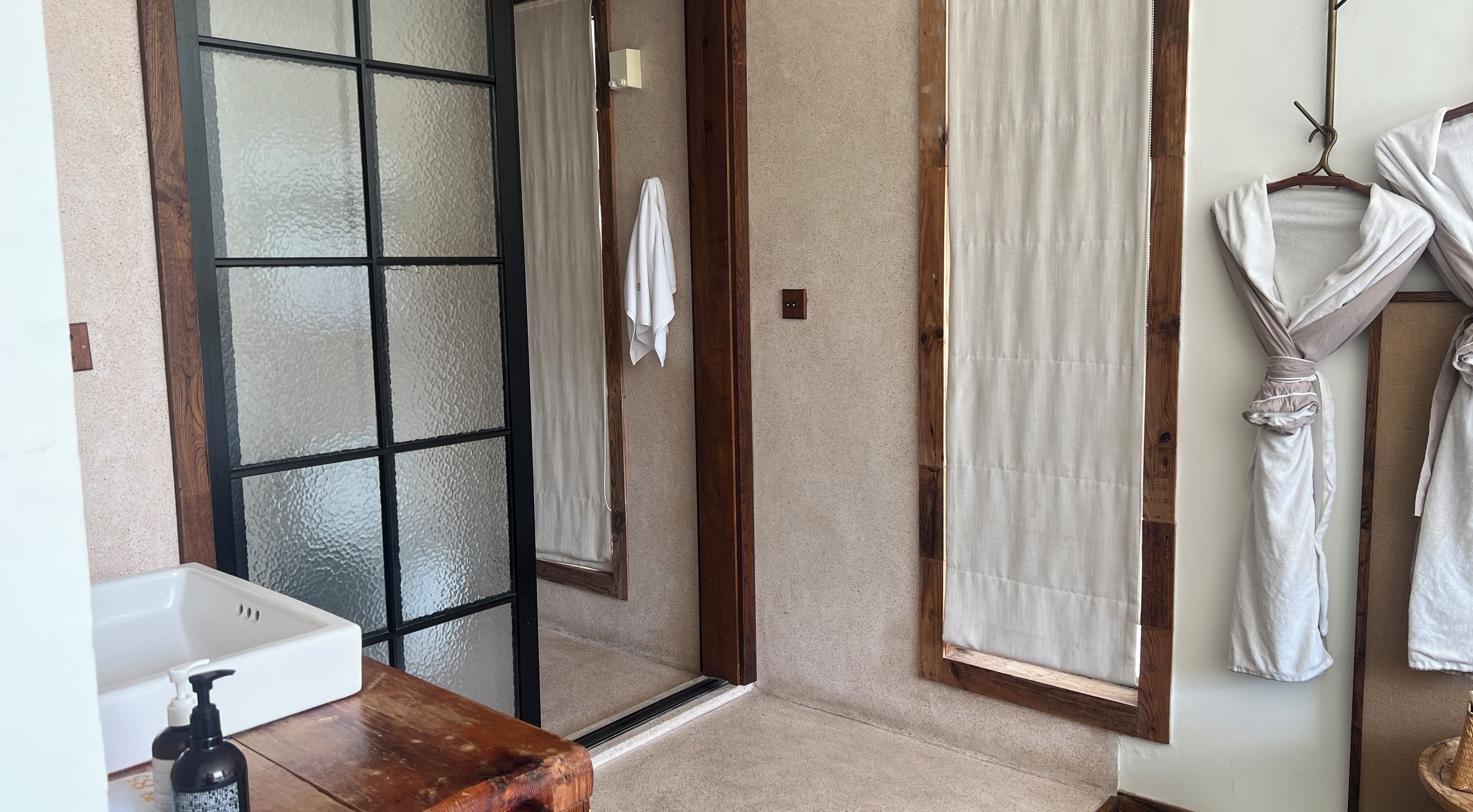 A bathroom with a glass door shower, a wooden vanity, and a towel rack with robes.