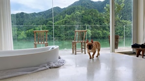 A room with a large bathtub, two wooden chairs, and a view of a lake and forest. - ZHU85 (Lishui)