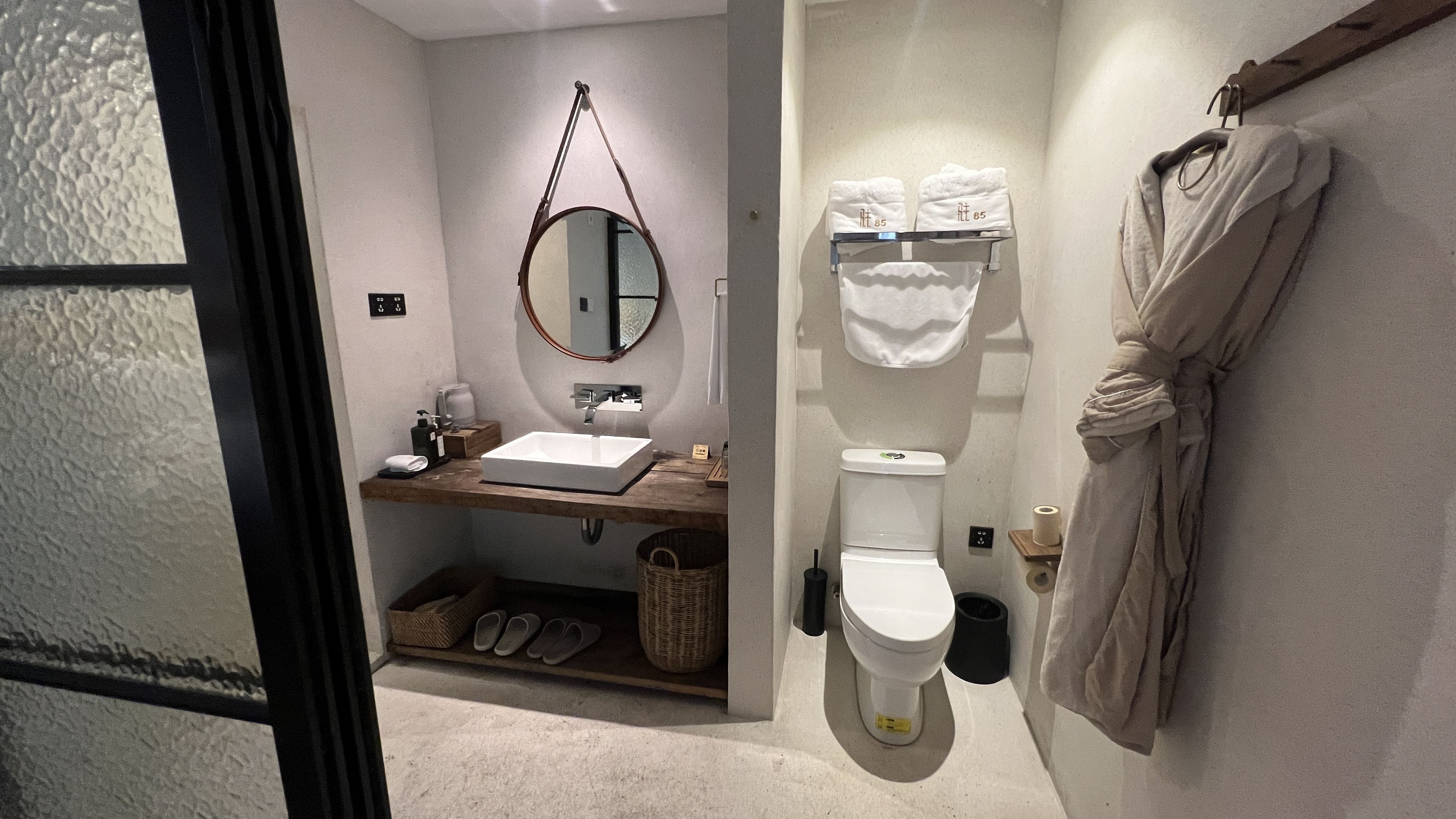 A modern bathroom with a sink, mirror, toilet, and a robe hanging on the wall.