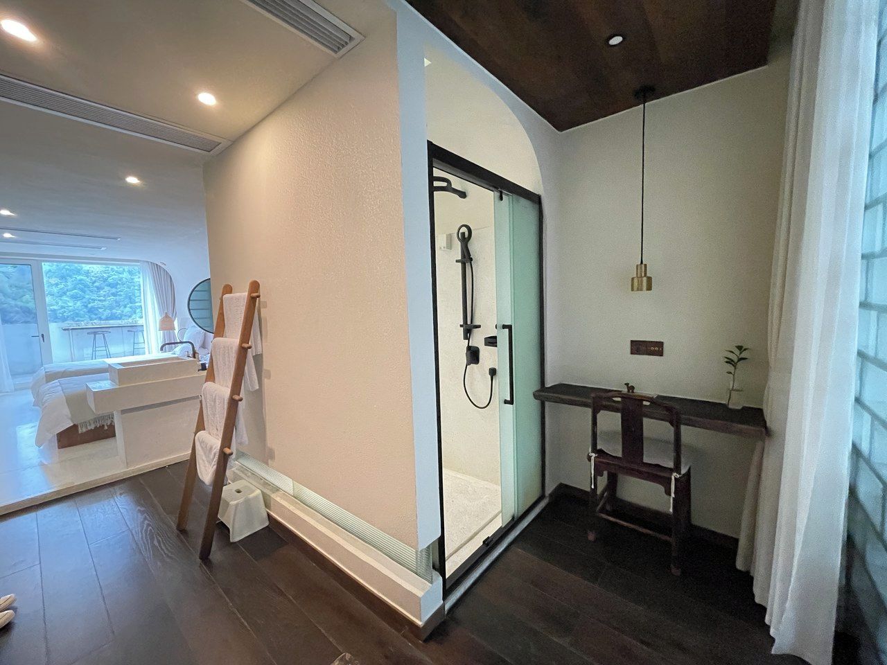 A modern bathroom with a glass shower enclosure, a wooden ladder, and a small wooden table.