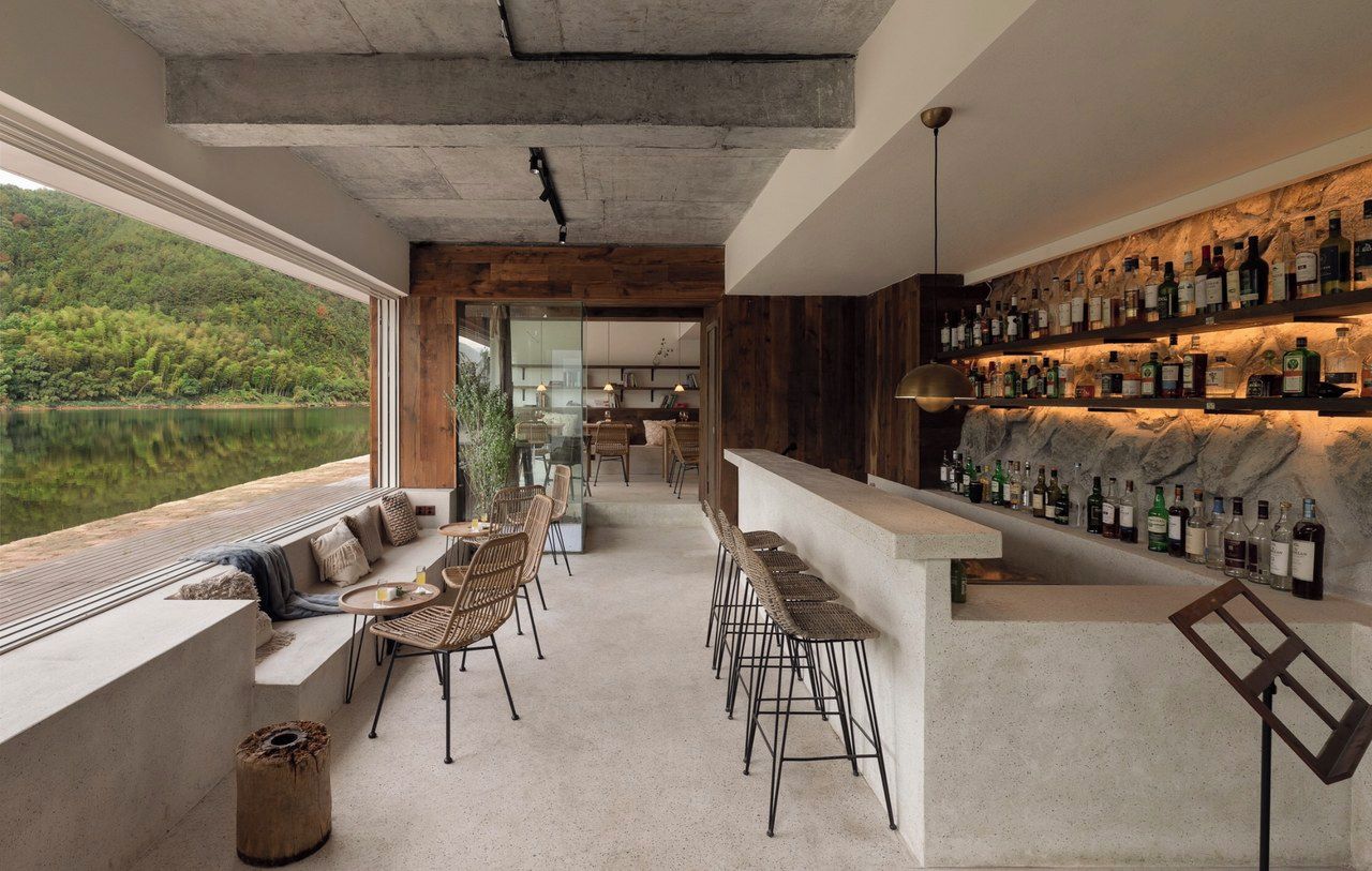A modern bar area with a long counter, bar stools, and a view of a lake.