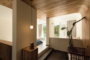 A room with a wooden ceiling, a bench, a chair, a table with a sculpture, and a view of greenery through a window. - ZHU85 (Lishui)