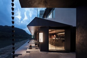 A modern building with a glass entrance, outdoor seating, and a view of the water. - ZHU85 (Lishui)
