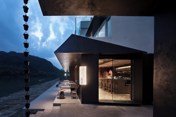 A modern building with a glass entrance, outdoor seating, and a view of the water. - ZHU85 (Lishui)