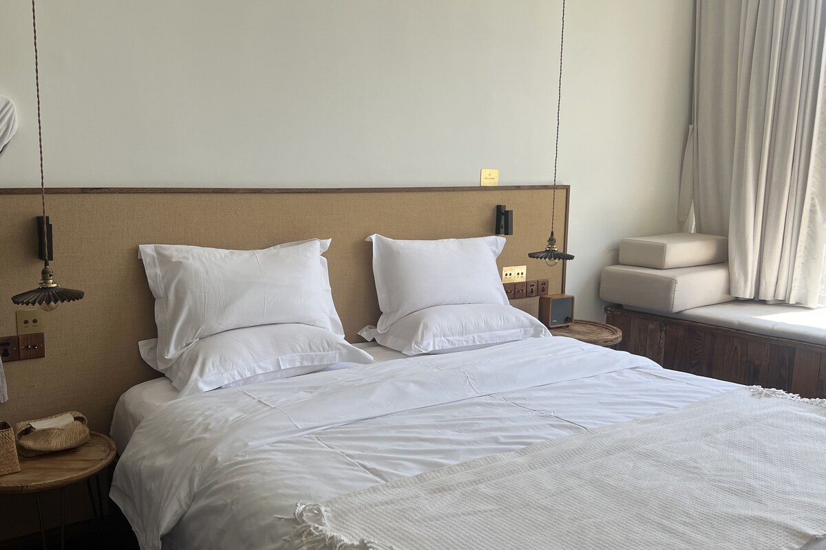A hotel room with a bed, bedside tables, a hanging robe, and a window with curtains.