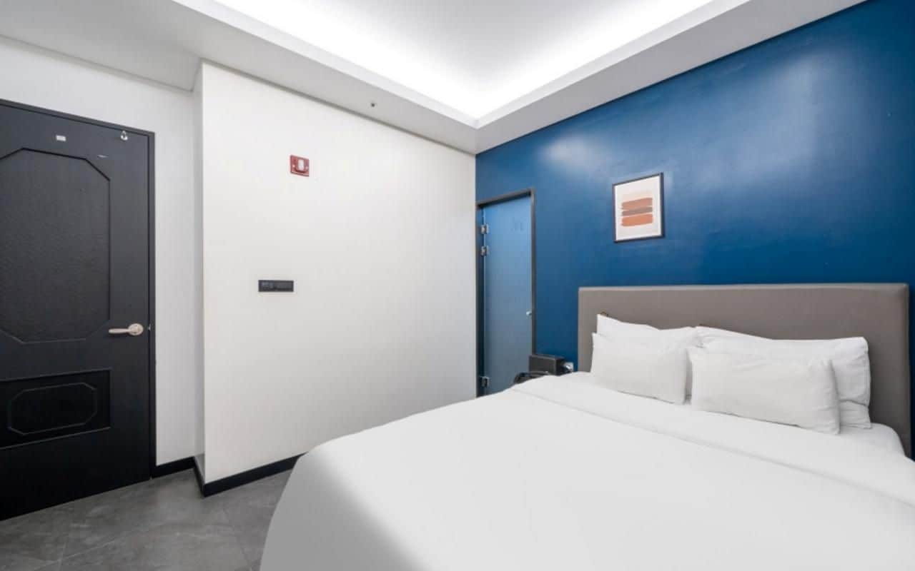 A hotel room with a bed, a door, and a blue accent wall.