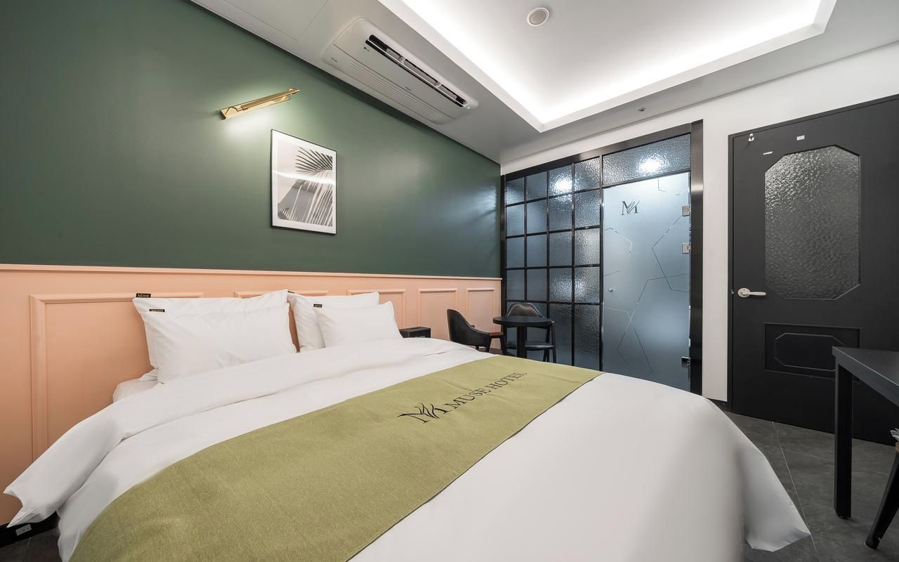 A hotel room with a bed, a desk, a chair, a framed picture on the wall, and a door with frosted glass panels.