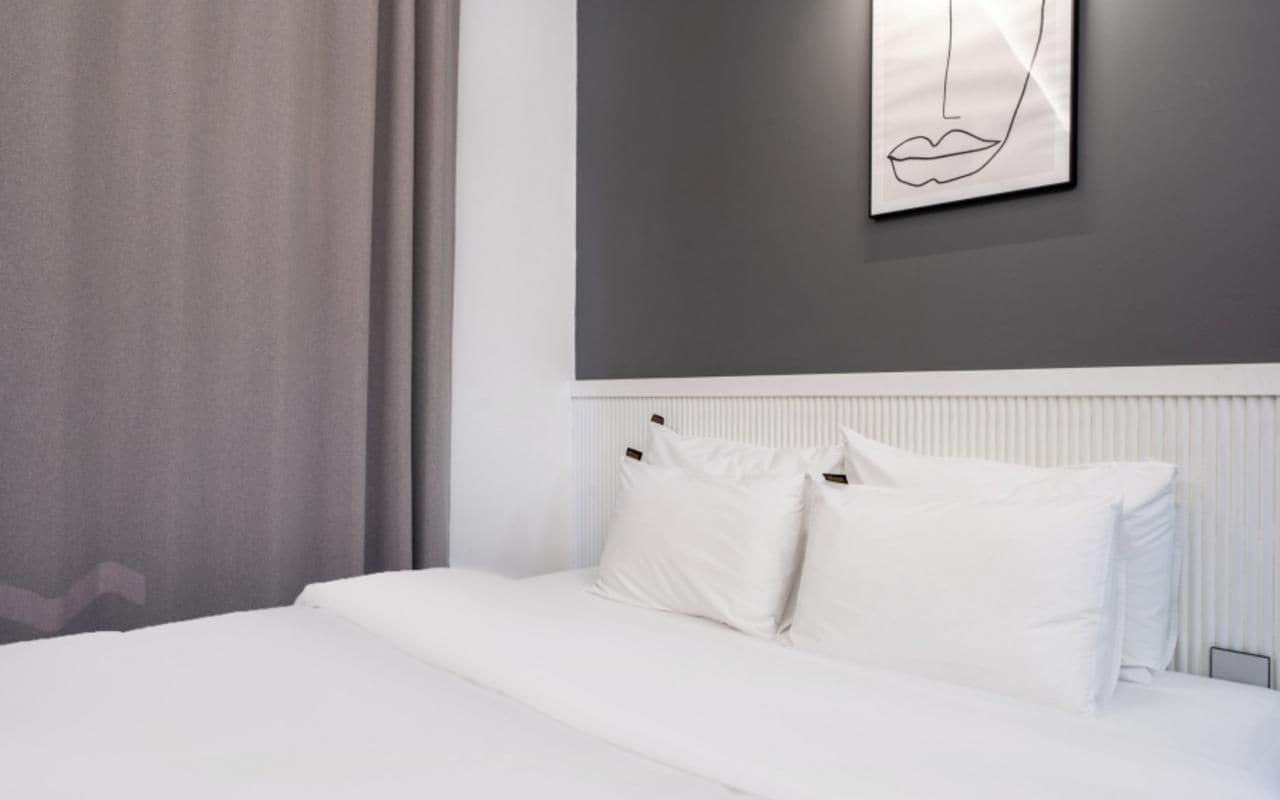 A modern hotel room with a large bed, white bedding, a radiator, and a wall-mounted artwork.
