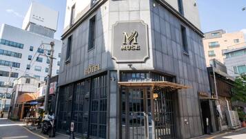 Un edificio en esquina con un letrero que dice 'MUSE', un letrero que dice 'HOTEL' y una entrada con portón.