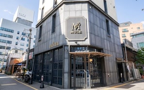 A corner building with a 'MUSE' sign, a 'HOTEL' sign, and a gated entrance.