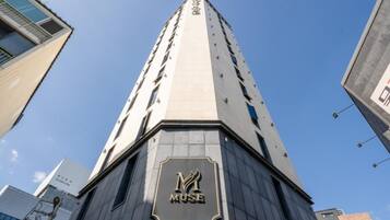 Un edificio alto con un llamativo letrero 'MUSE' en la base, rodeado de otros edificios modernos.