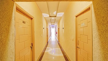 A hotel corridor with doors on both sides, a marble floor, and a ceiling with recessed lighting.