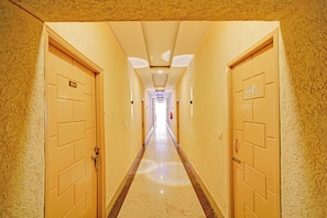 Pasillo de hotel con puertas a ambos lados, piso de mármol e iluminación empotrada en el techo.