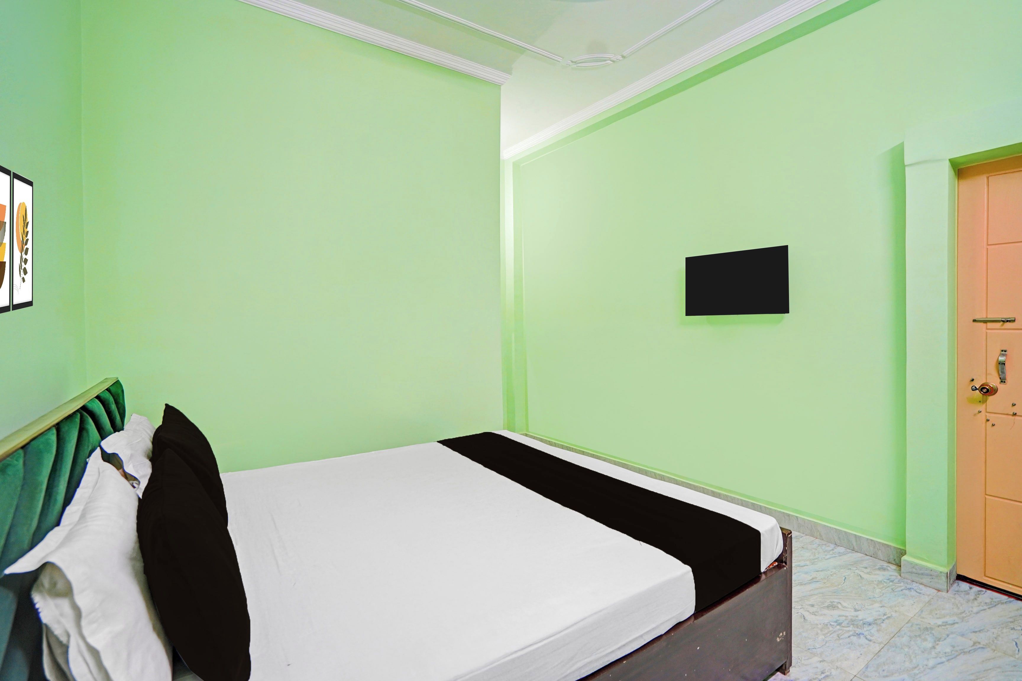 A room with a bed, a door, a wall-mounted TV, and a framed picture.