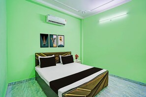 A room with a bed, a nightstand, a vase with flowers, and wall art. - Hotel O JP International Airport Patna (Danapur)