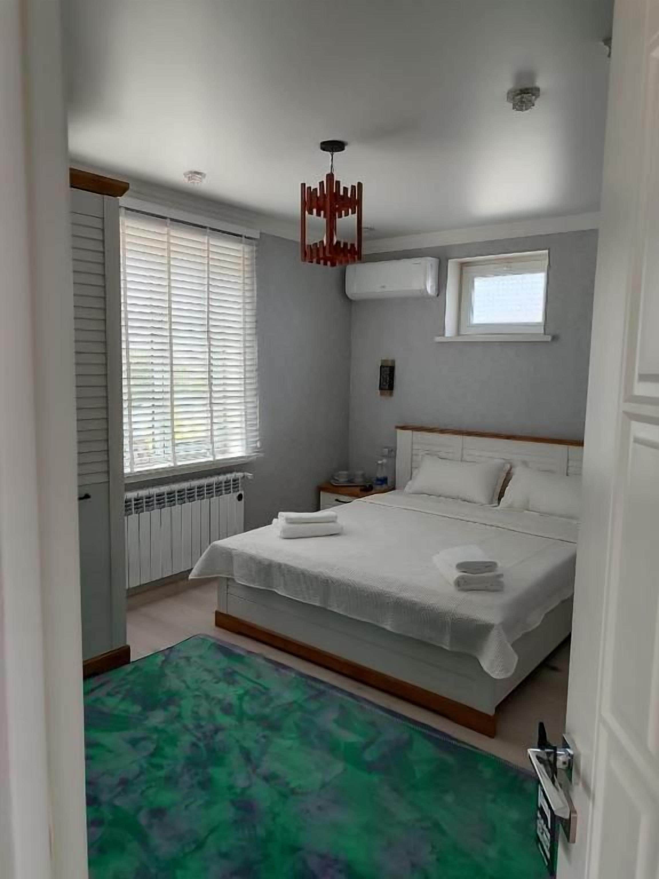 Ein Schlafzimmer mit einem Bett, einem Fenster mit Jalousien, einem Heizkörper und einem grünen Teppich.
