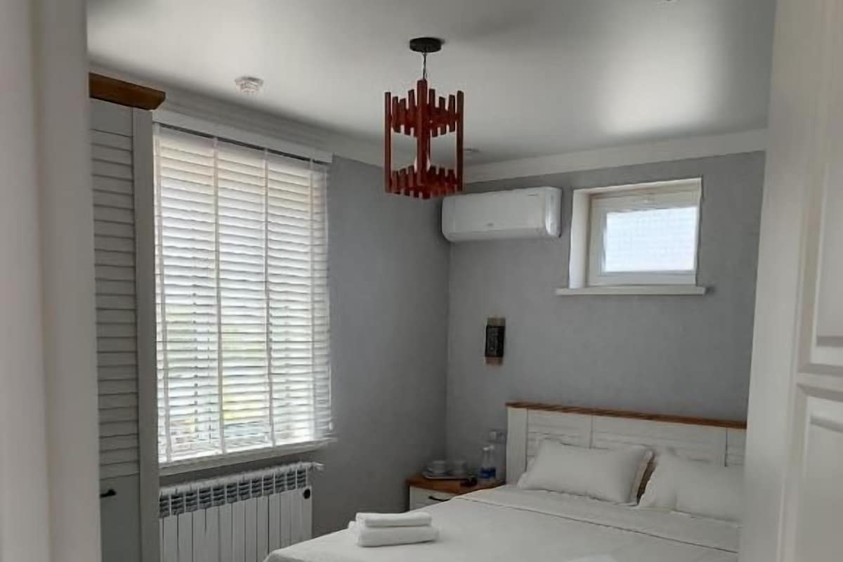 Un dormitorio con cama, ventana con persianas, radiador y alfombra verde.