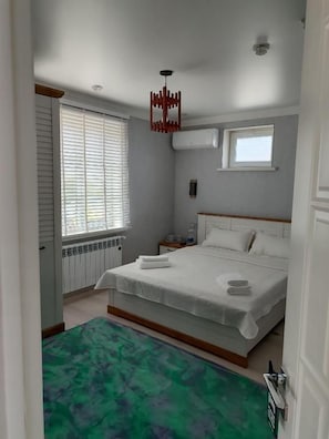 A bedroom with a bed, a window with blinds, a radiator, and a green rug.