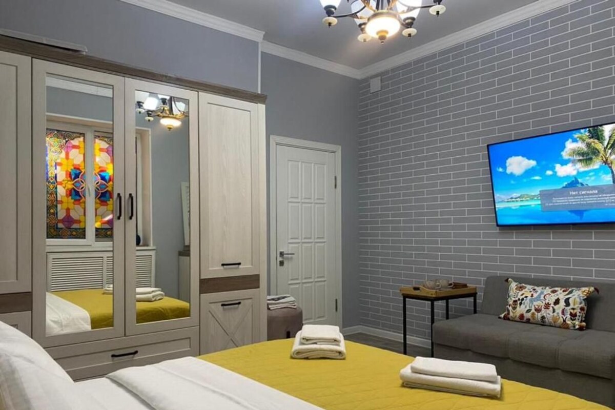 A hotel room with a bed, a sofa, a TV, a wardrobe, and a mirror.