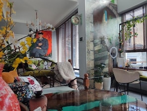 A room with a dining table, chairs, a sofa, a decorative vase, a clock, and a window with blinds. - The Oldman House (Osh)