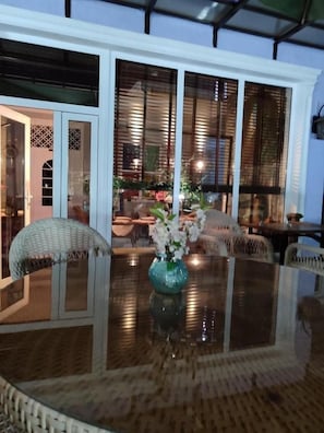 A dining area with a glass table, wicker chairs, and a vase with flowers. - The Oldman House (Osh)