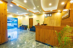 A hotel lobby with a reception desk, seating area, and a pool view. - Hotel Quest (Pokhara)