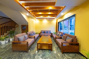 A lobby with a wooden ceiling, a central coffee table, and sofas arranged around it. - Hotel Quest (Pokhara)