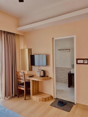 A hotel room with a bed, a desk with a chair, a television, and a bathroom visible through an open door. - Hotel Quest (Pokhara)
