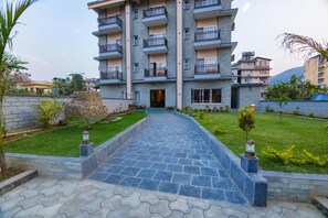 A multi-story residential building with balconies, a paved entrance, and a landscaped garden. - Hotel Quest (Pokhara)