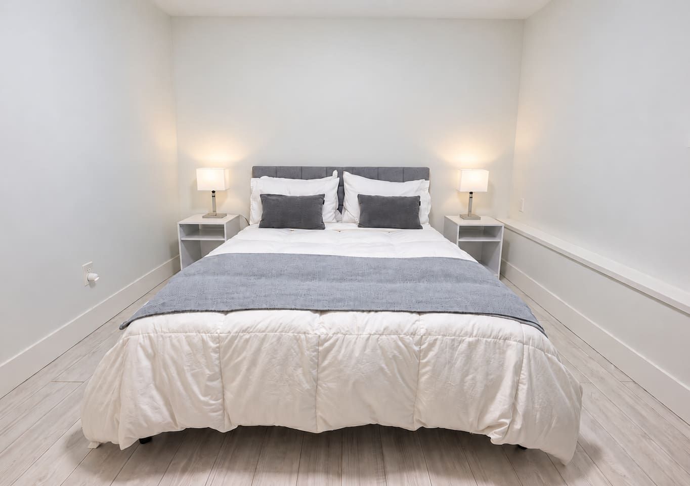 A modern bedroom with a large bed, two bedside tables with lamps, and a grey throw blanket.