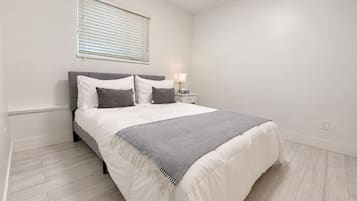 A bedroom with a bed, bedside table, lamp, and a window with blinds.